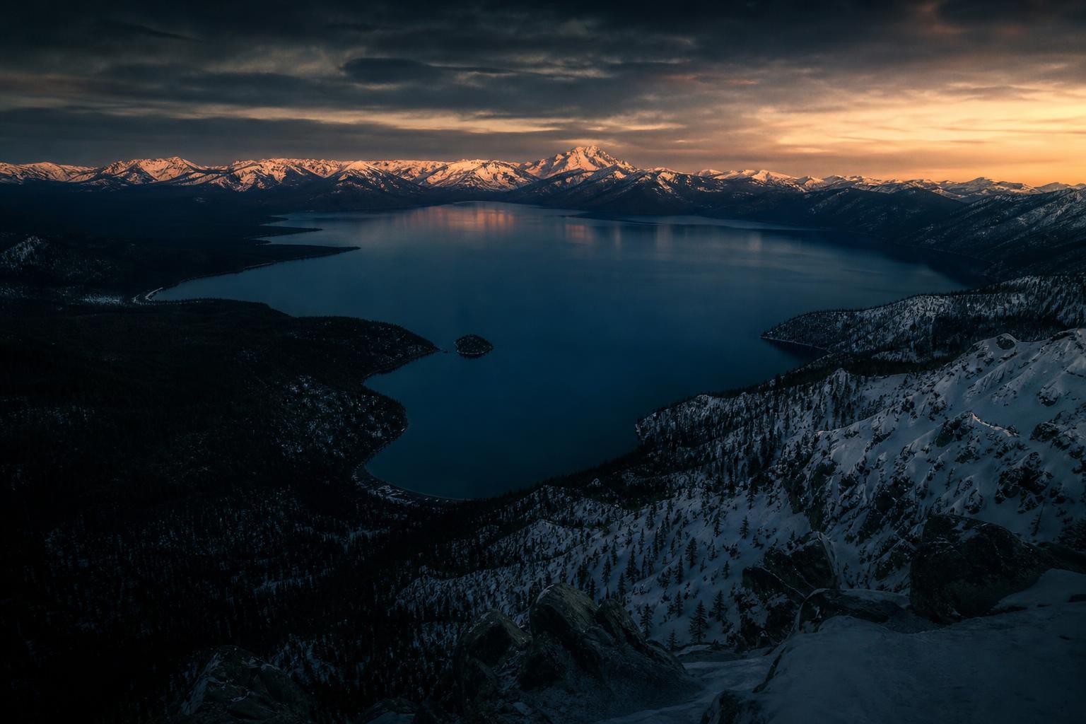 Lake Tahoe at dusk — snow-capped Sierra Nevada mountains surrounding deep blue alpine water